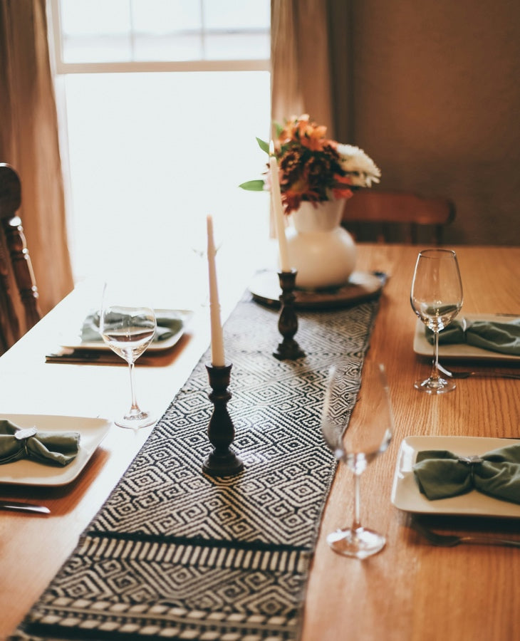Textured table runner styled with candles and place settings in a warm dining room