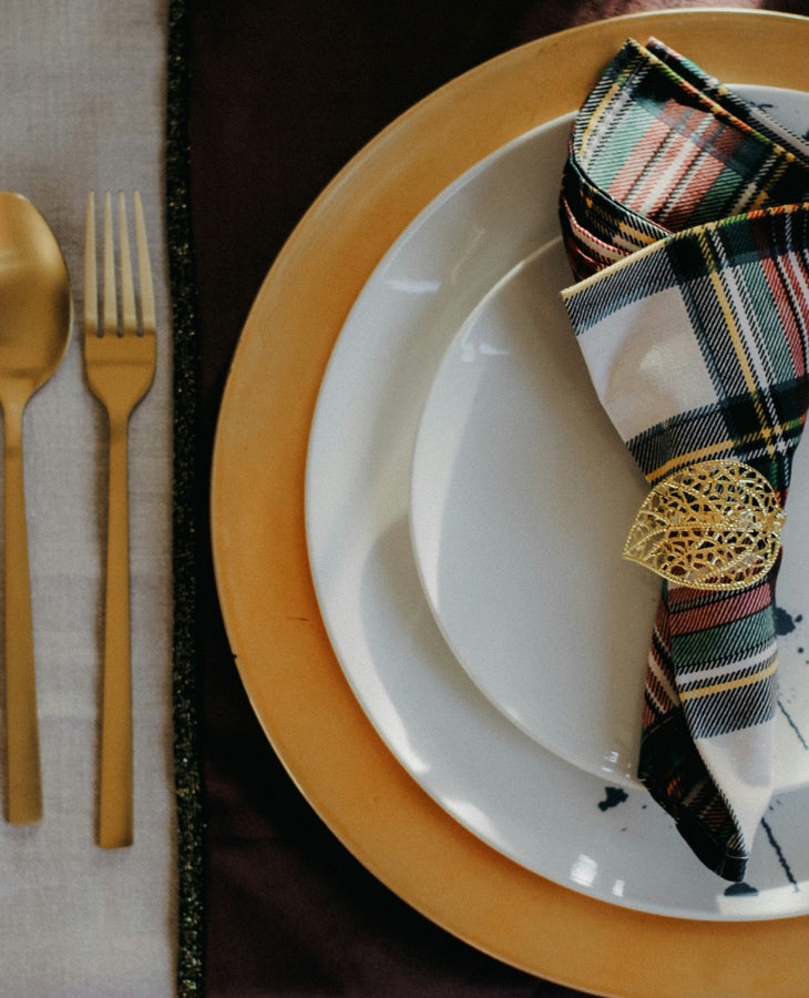 Layered dinner plates with gold flatware, a plaid napkin, and an ornate napkin ring